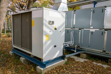 Commercial air handling unit with big condensing unit standing outdoor on the ground covered by fallen leaves